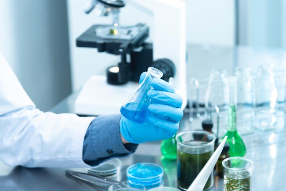 clinical lab technician holding a beaker of blue liquid while working in a lab