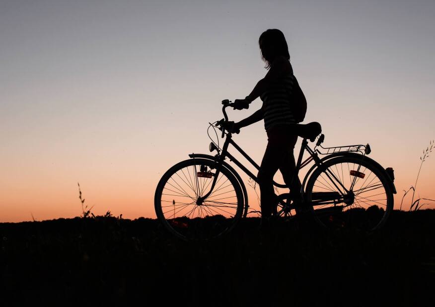 silhouette of a woman walking a bicycle through an open field at dusk