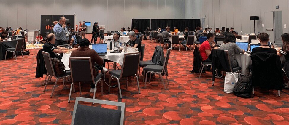 conference participants on their laptops at several tables in a large ballroom