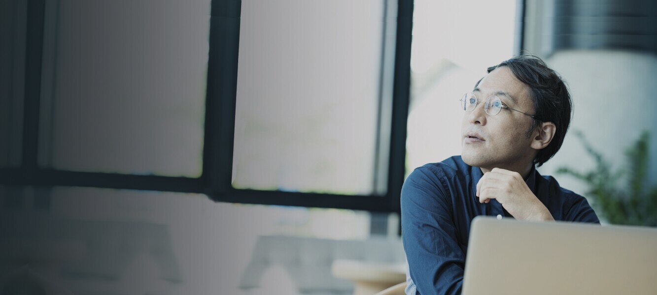 Asian businessperson using his laptop and thinking about business plan in an office