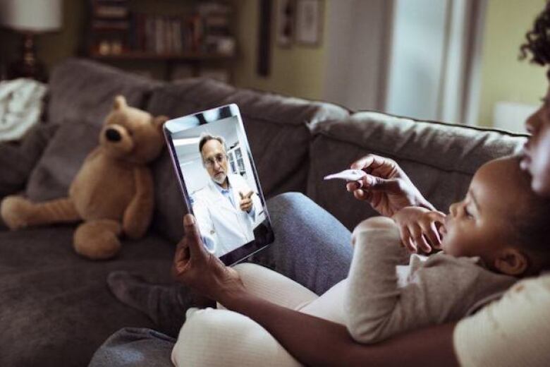doctor on tablet talking to a caregiver holding a baby and a thermometer