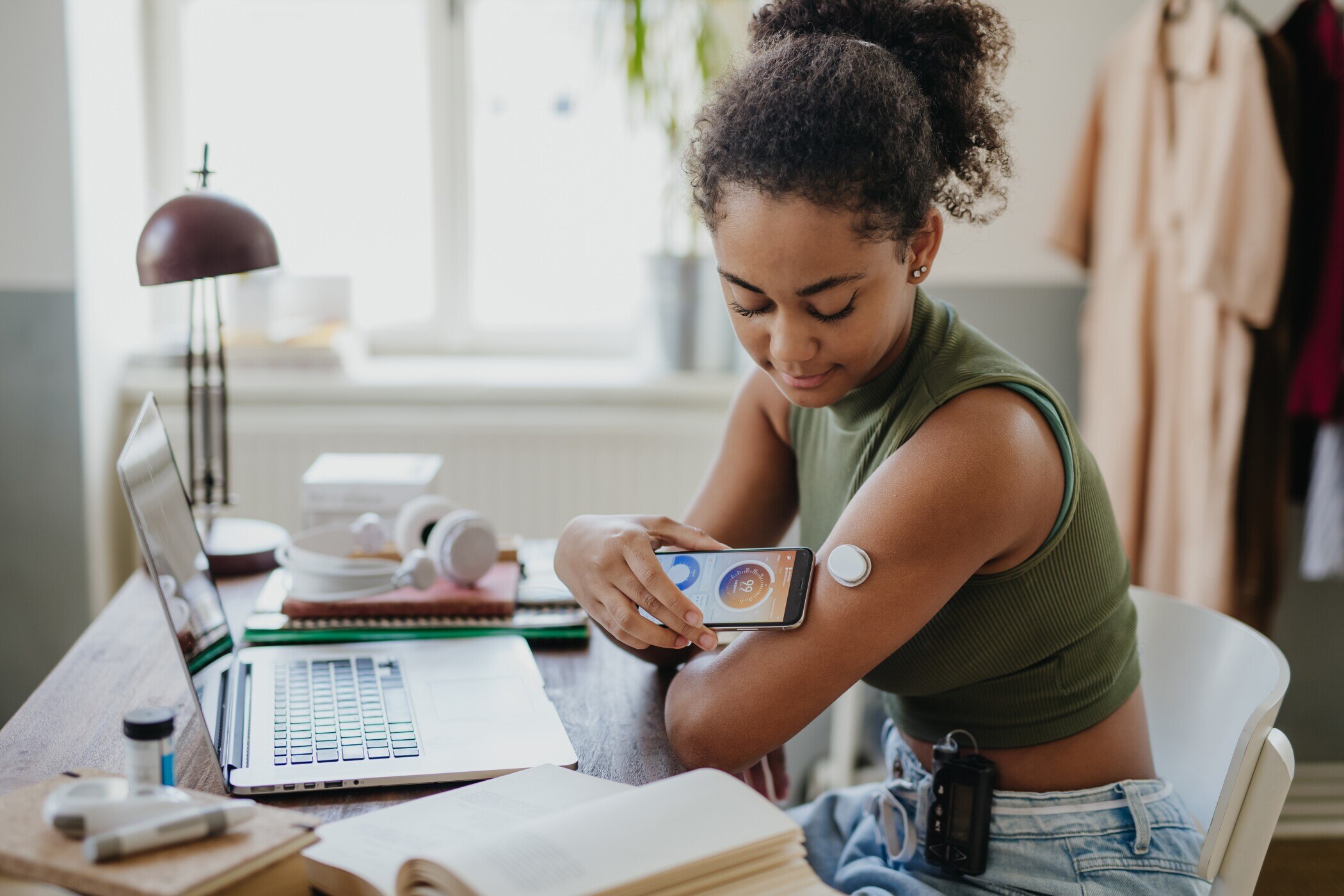 Teenage girl connecting smartphone to continuous glucose monitor, checking blood glucose during day.