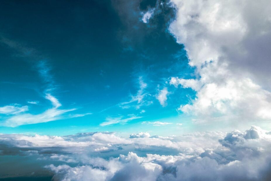Airplane-level view of fluffy white and gray clouds in a turquoise-blue sky