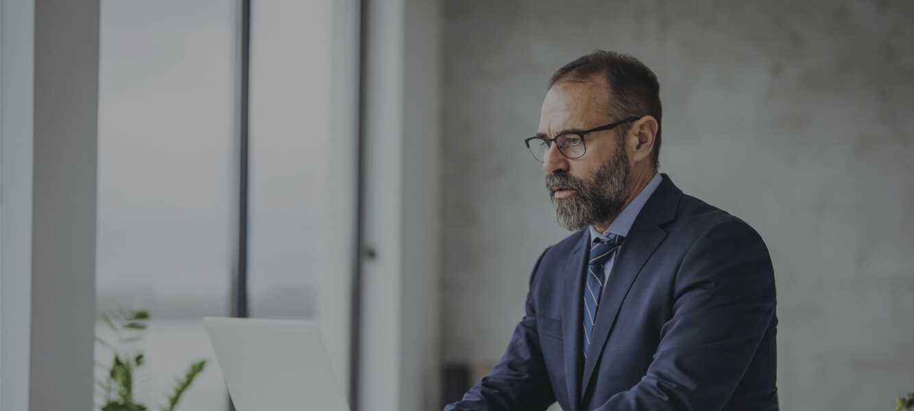Older, bearded businessman sitting at his desk, working on his laptop