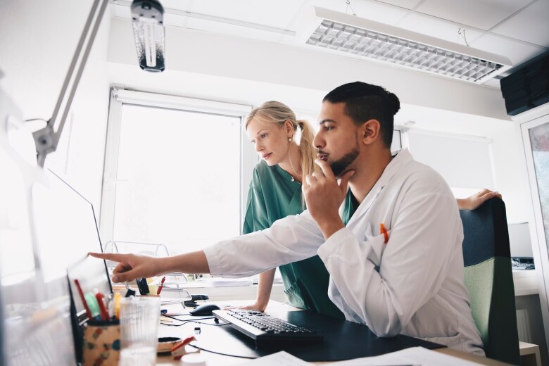 Young male doctor pointing at computer monitor to female nurse in office