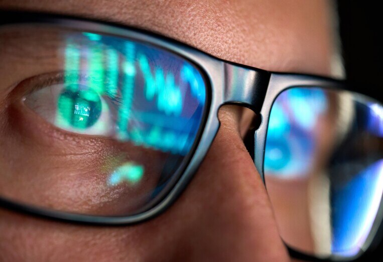Close-up of a person wearing glasses with financial charts reflected in the lenses.