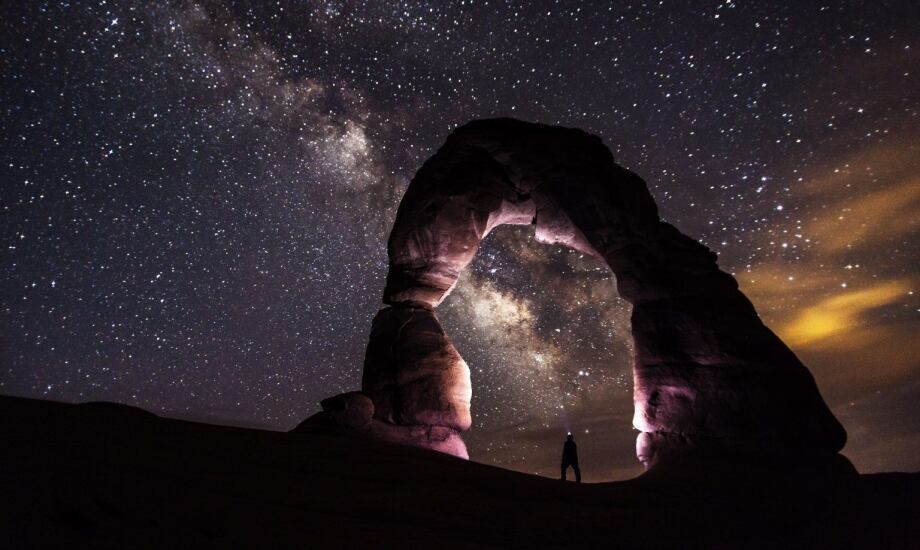 standing under an arch rock formation looking up at the night sky full of stars