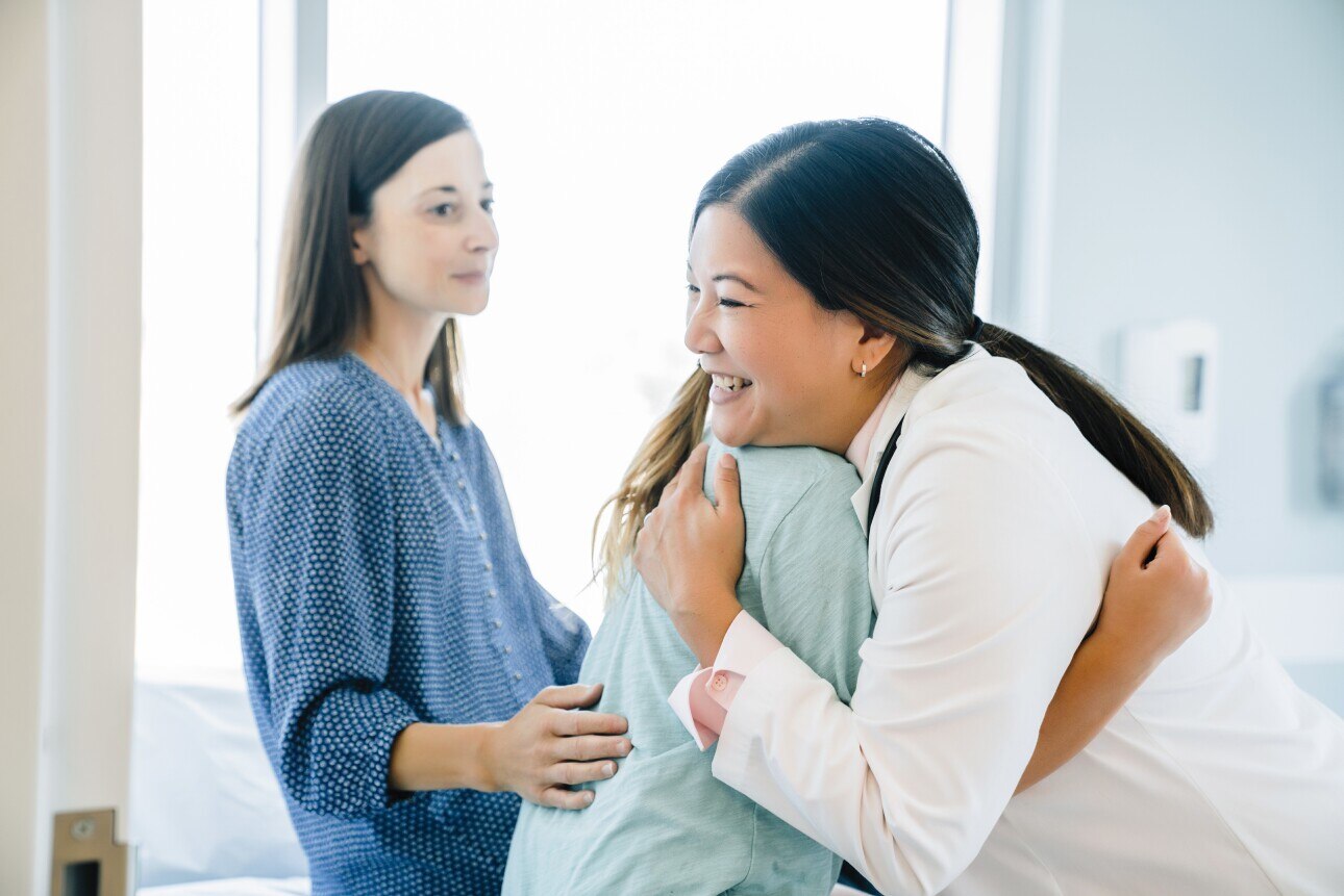 Female doctor hugging young patient next to mother