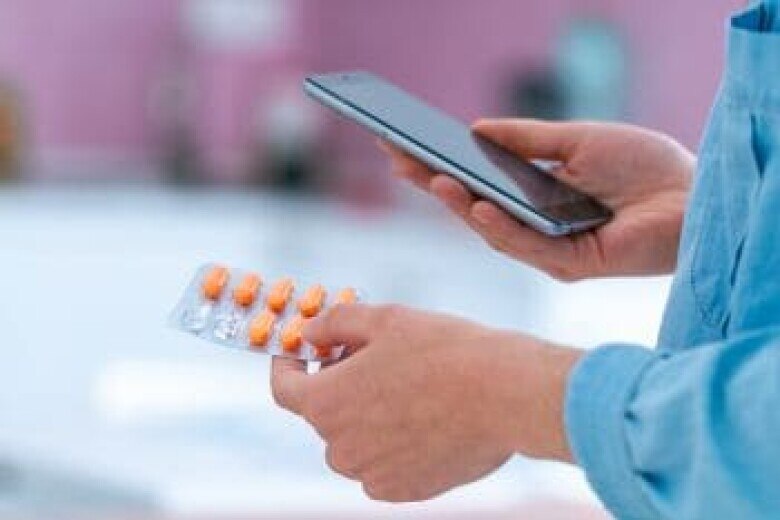 person holding medication and checking their mobile phone