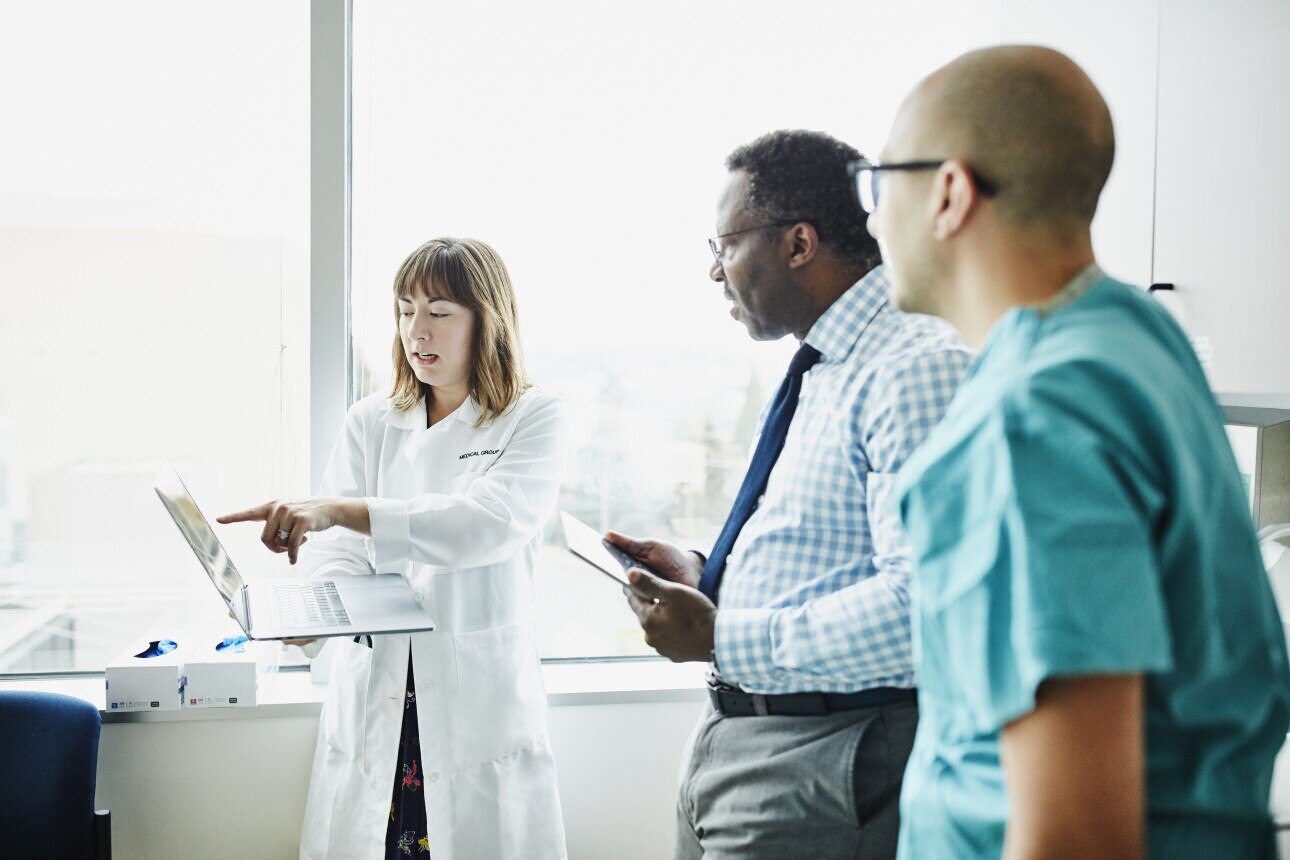 Female doctor holding laptop discussing patient information with medical team in exam room