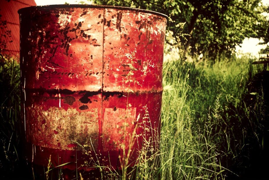 red, rusty garbage can in a filed of overgrown grass