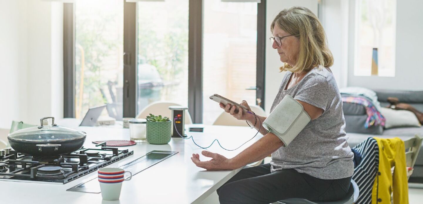 Patient Woman at home checking blood pressure with medical device - healthcare