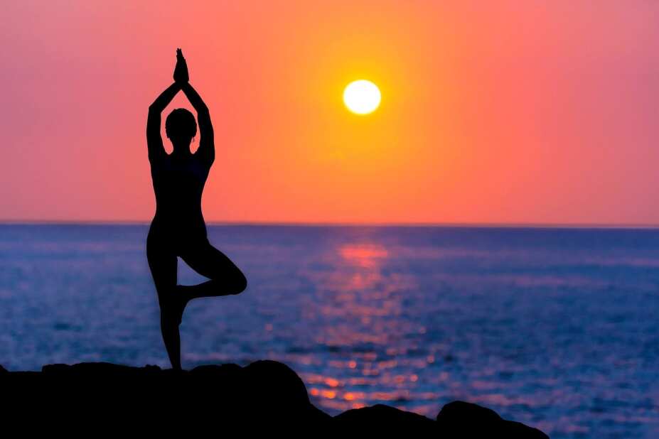silhouette of a woman doing a tree pose from yoga, overlooking a colorful pink and orange sunset over the blue ocean