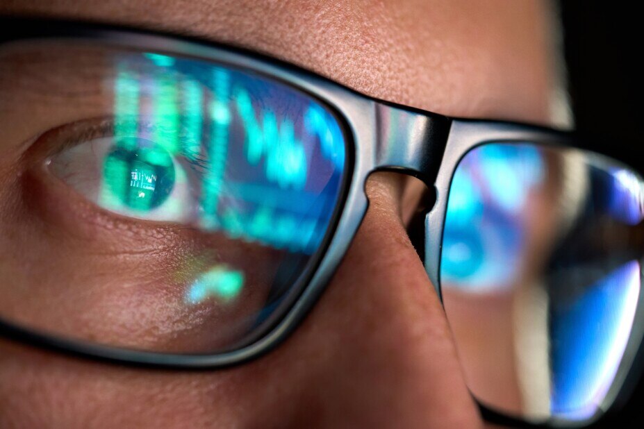 Close-up of a person wearing glasses with financial charts reflected in the lenses.