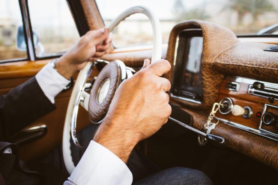 A man's hands on the steering wheel of a vintage car