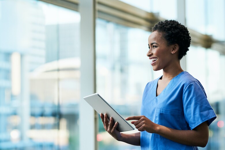 smiling nurse using tablet in hospital hallway