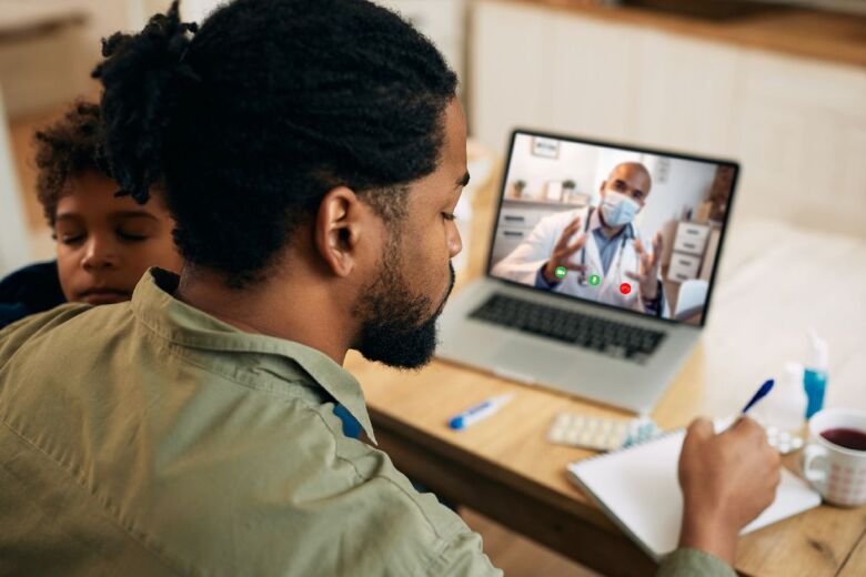 father holding young son while on a telehealth call with the peditrician