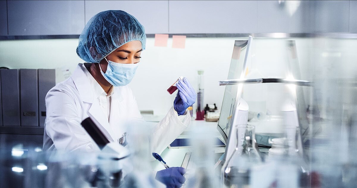 lab tech holding a vial of liquid and taking notes