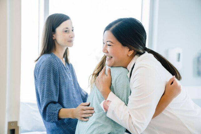 Female doctor hugging young patient next to mother