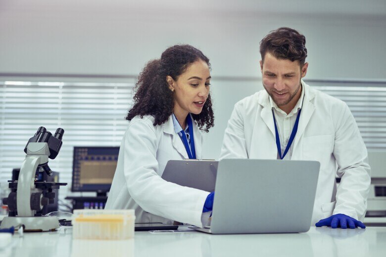 Female scientist and male colleague smiling and discussing work on laptop in laboratory