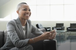 smiling businesswoman using cell phone on sofa in office