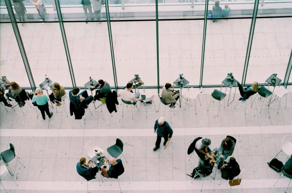colleagues at several small tables, having a bite to eat in the café of their office
