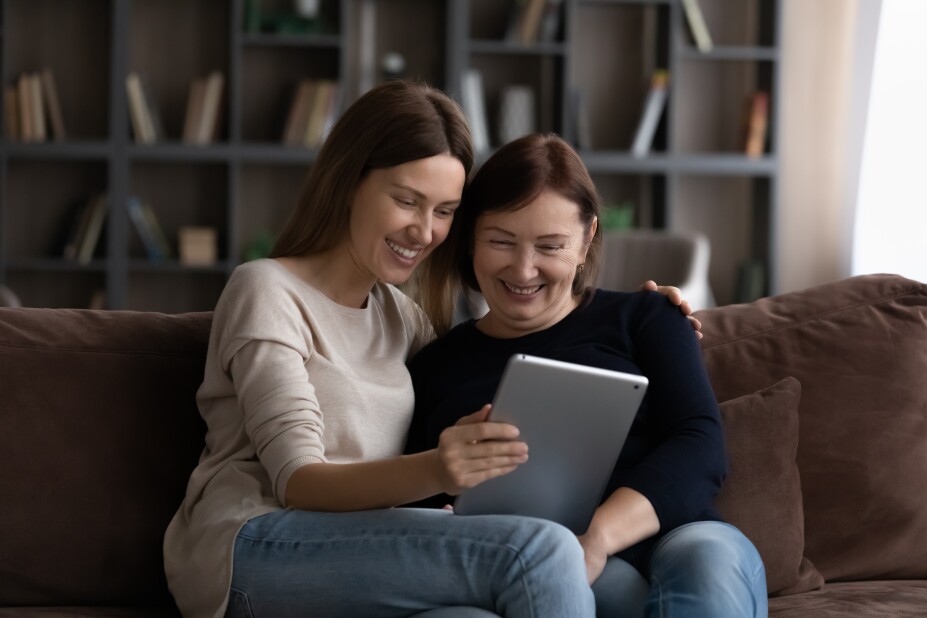 Happy grownup daughter showing content on a tablet to her mature mother