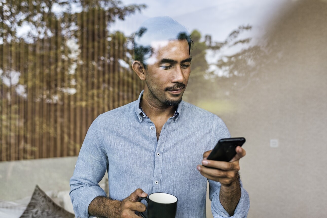 Asian businessman working from home, using smartphone and drinking coffee