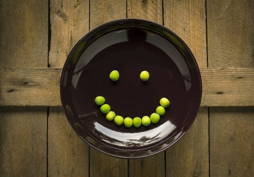 brown plate with a smiley face made of green chickpeas