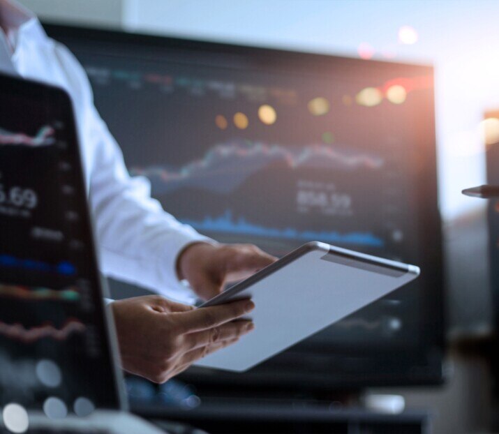 Businessman using tablet for analyzing data stock market in monitoring room with team pointing on the data presented in the chart on screen