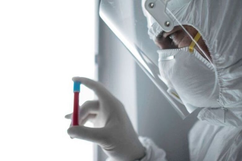 lab technician in full personal protective equipment looking at vial of blood