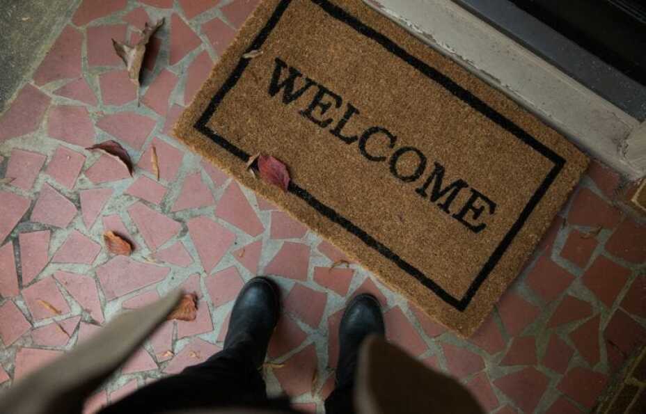 person pauses before a welcome mat at a doorstep