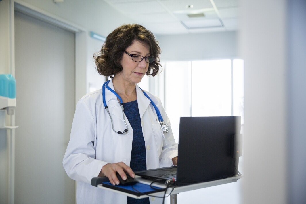 Mature female doctor using laptop in hospital corridor