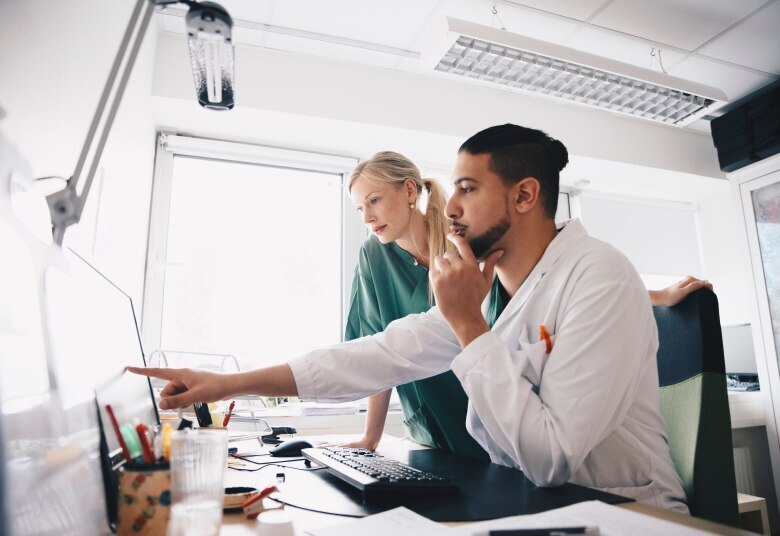 Young male doctor pointing at computer monitor to female nurse in office