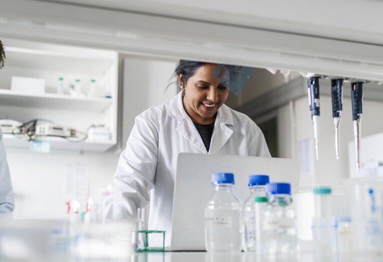 Smiling scientist using laptop in laboratory