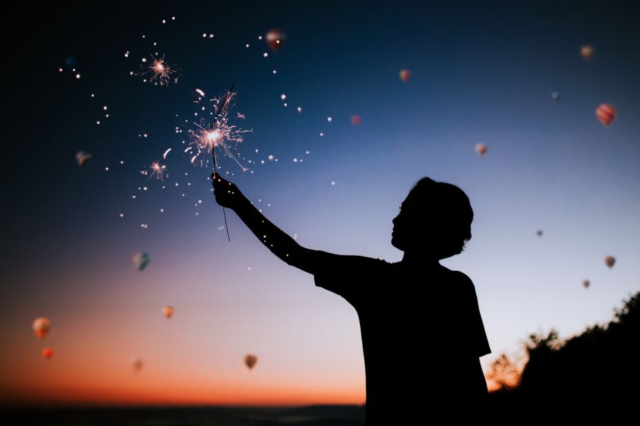 silhouette of a child holding a sparkler with a sky full of hat air balloons in the background