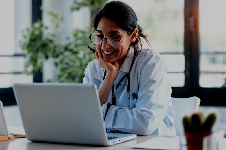 Smiling female doctor working with her laptop in the consultation.