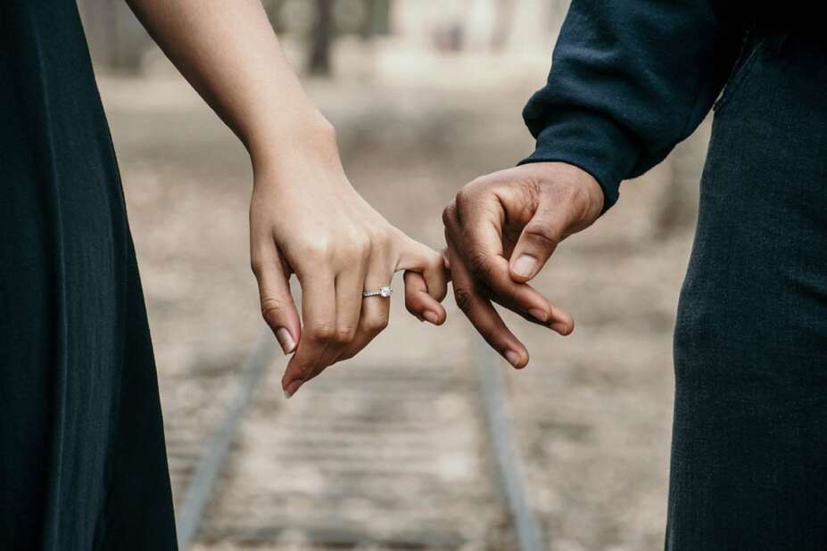 engaged couple interlocking pinky fingers while walking along old railroad tracks