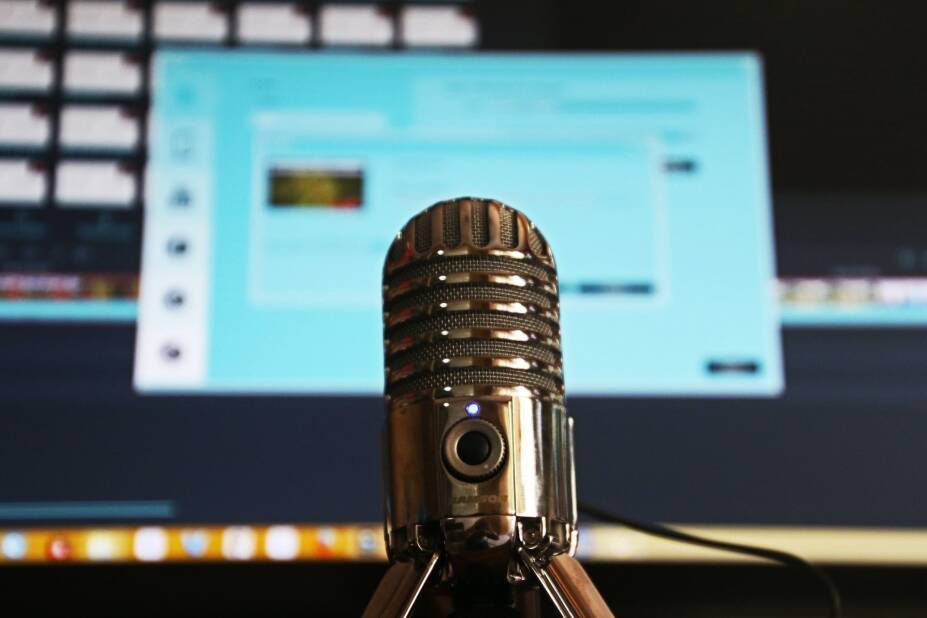 classic-style microphone in focus in front of an out-of-focus computer monitor