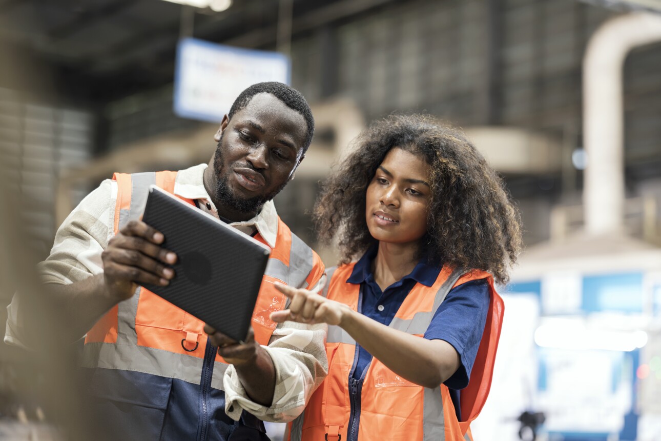 African American Production Control Engineers standing on the shop floor reviewing daily report on a tablet