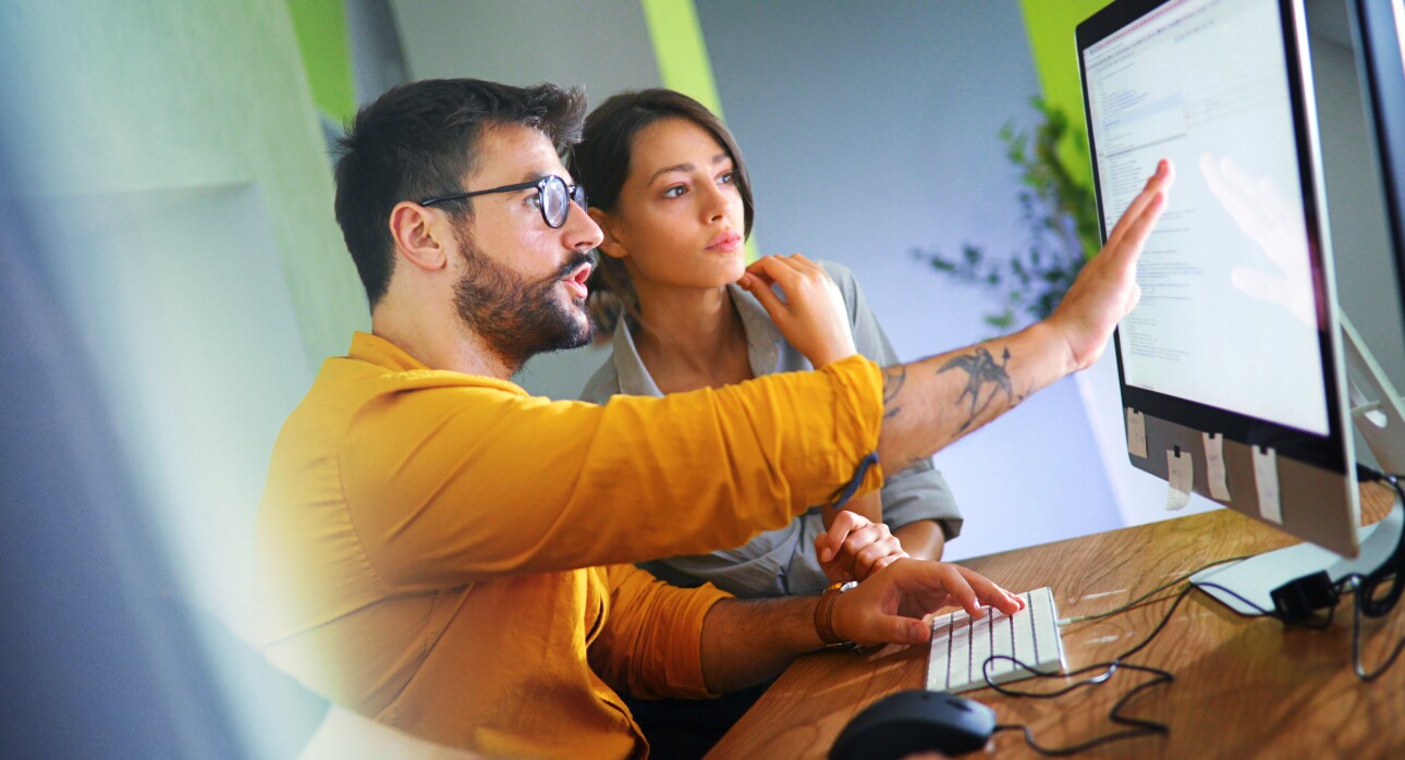 Closeup side view of couple of mid 20's software developers resolving some issues with the code they're currently working on.