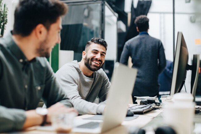 developers laughing and sitting at table with laptops