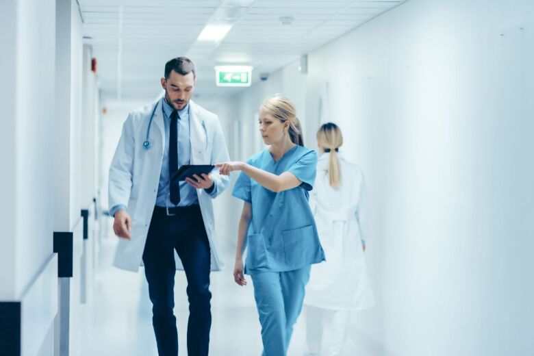 nurse showing doctor information on a tablet while walking down hospital hallway