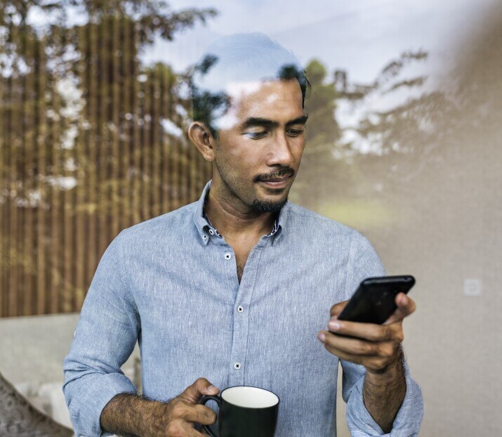 Asian businessman working from home, using smartphone and drinking coffee
