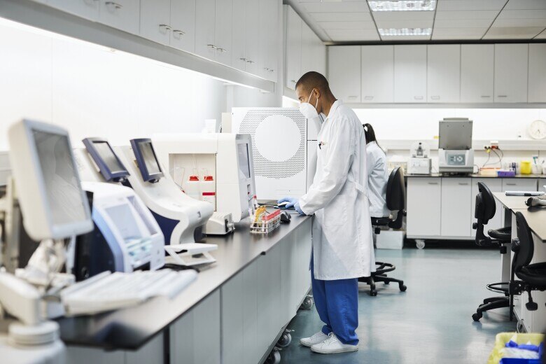 Male medical professional using computer in laboratory. Doctor is working in hospital during coronavirus outbreak. He is wearing protective face mask and uniform.