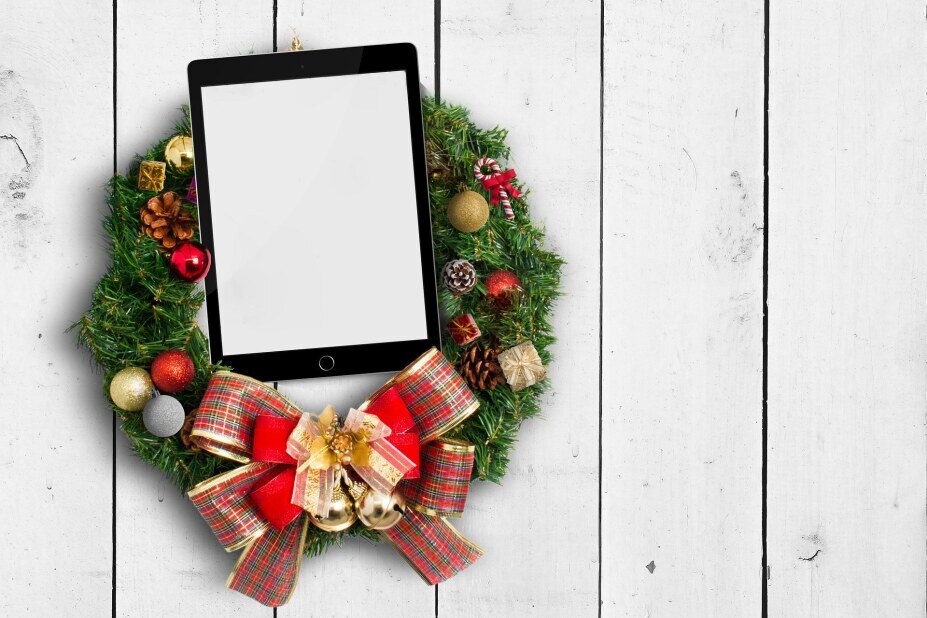 holiday wreath hanging on a white, wooden door with a tablet in the middle