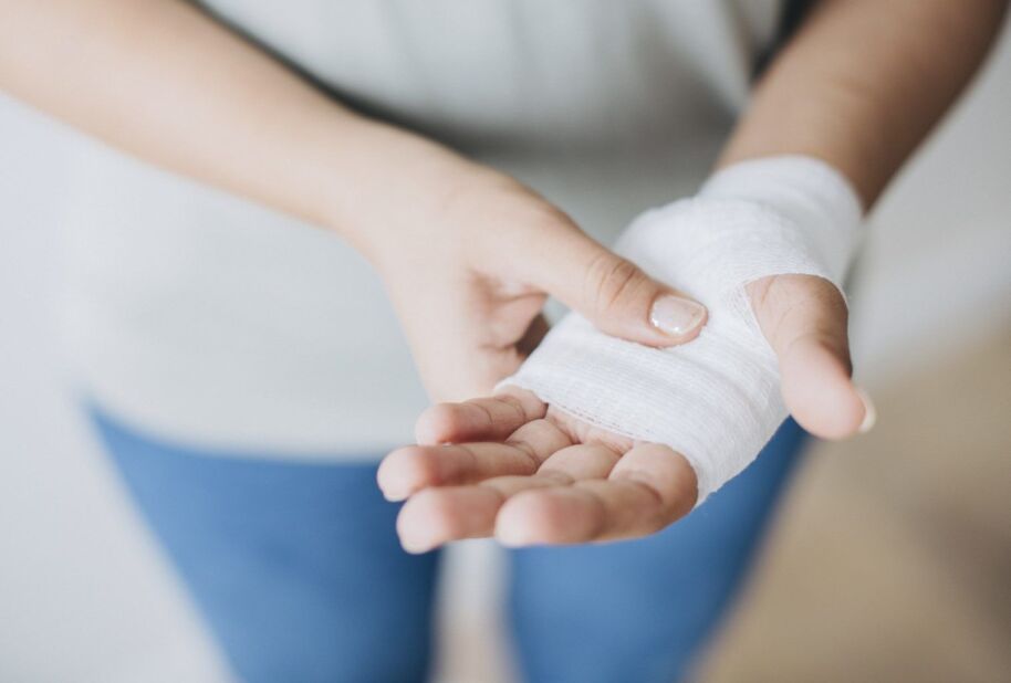 woman gently holds her injured hand wrapped in gauze