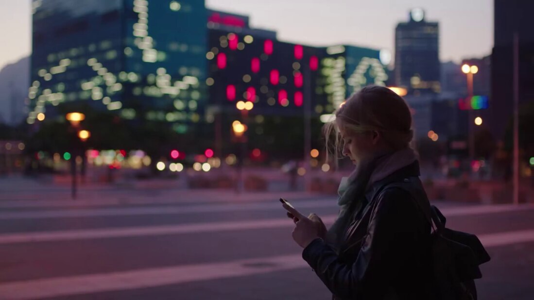 young woman outside in an urban setting at dusk looking at her phone