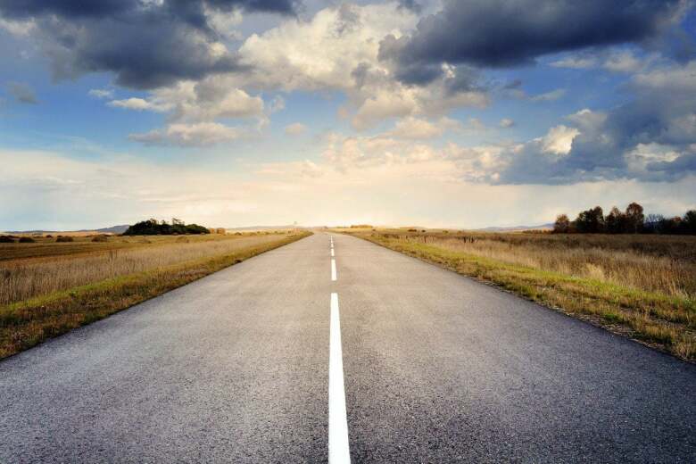 looking down a straight, empty road to the horizon under a blue, cloudy sky
