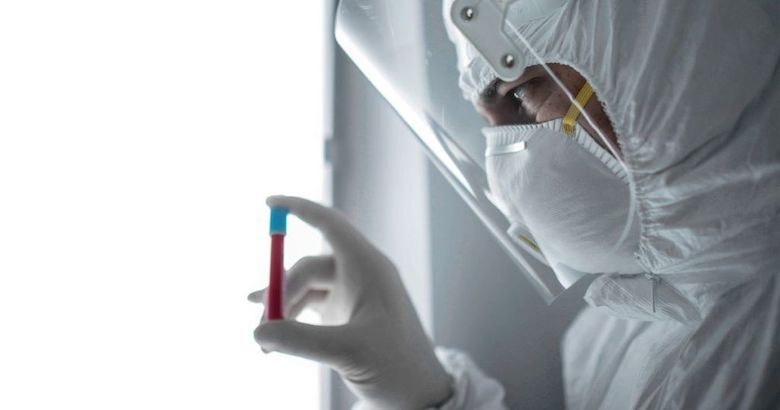 lab technician in full personal protective equipment looking at vial of blood
